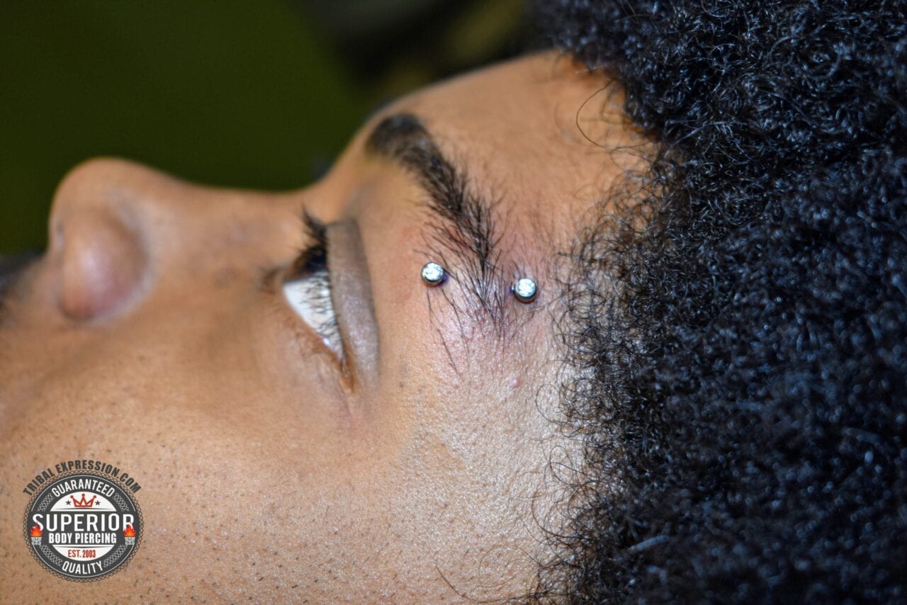Eyebrow Piercing on Deeper Skin Tone with Bright Titanium Jewelry – Tribal Expression Calgary Brow piercing with a NeoMetal titanium threadless curved barbell with forward facing CZ beads
