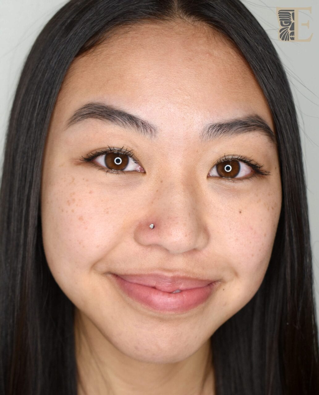 Face-on photo of a person smiling ear to ear with a beautifully placed nostril piercing featuring a small nose stud, done at Tribal Expression professional body piercing studio in Calgary