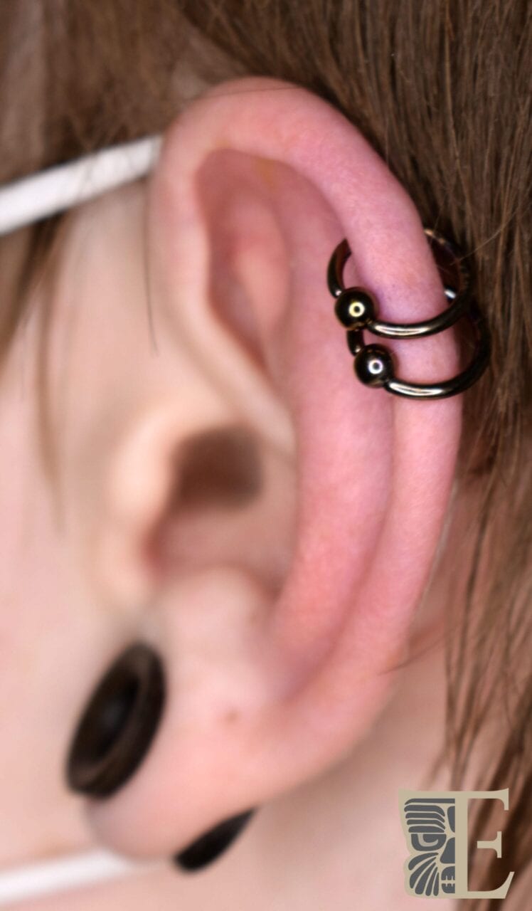 Side-profile close-up of a helix piercing with a Tribal Expression–made yellow gold disc end, crafted in Calgary from high-quality 14k gold