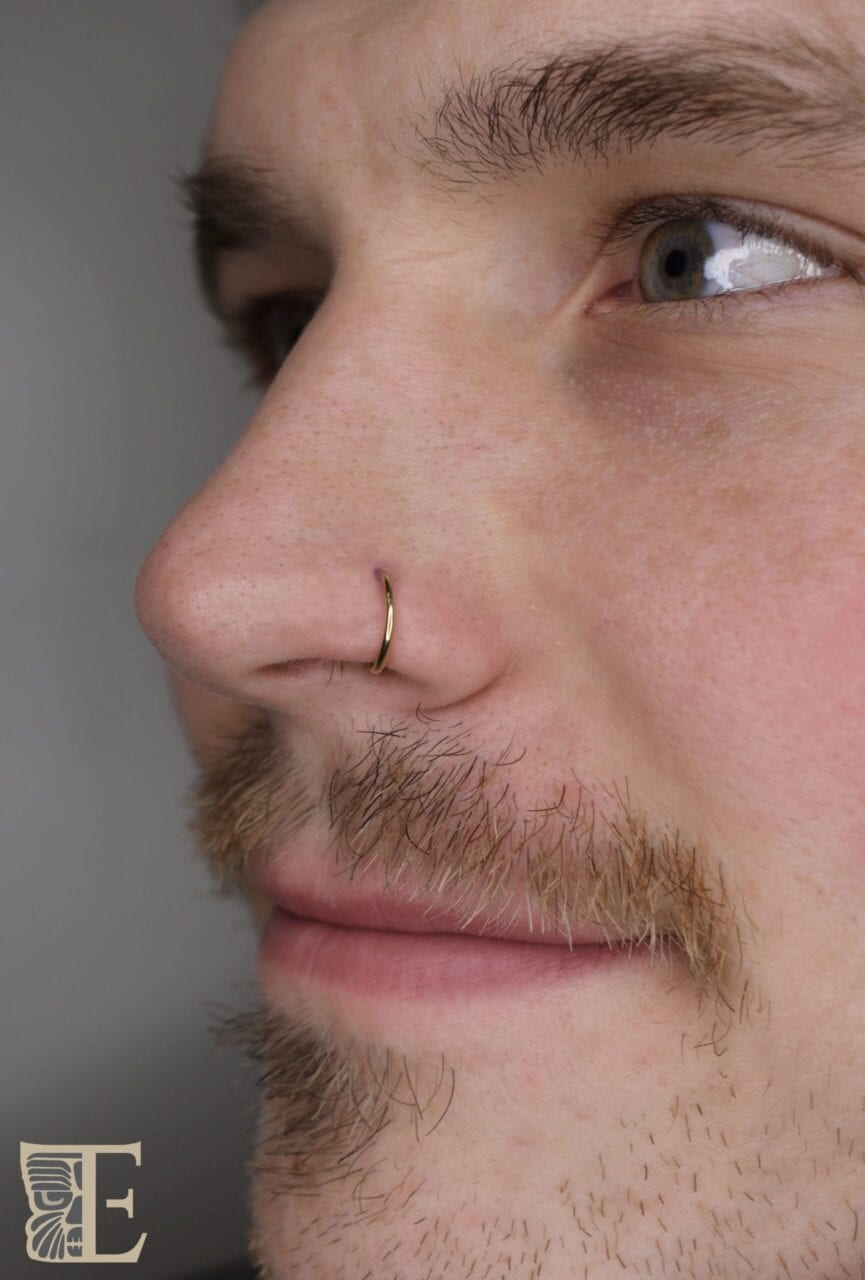 Side profile of a man with a classic nostril piercing wearing a simple high-polish titanium nose ring, professionally done at Tribal Expression in Calgary