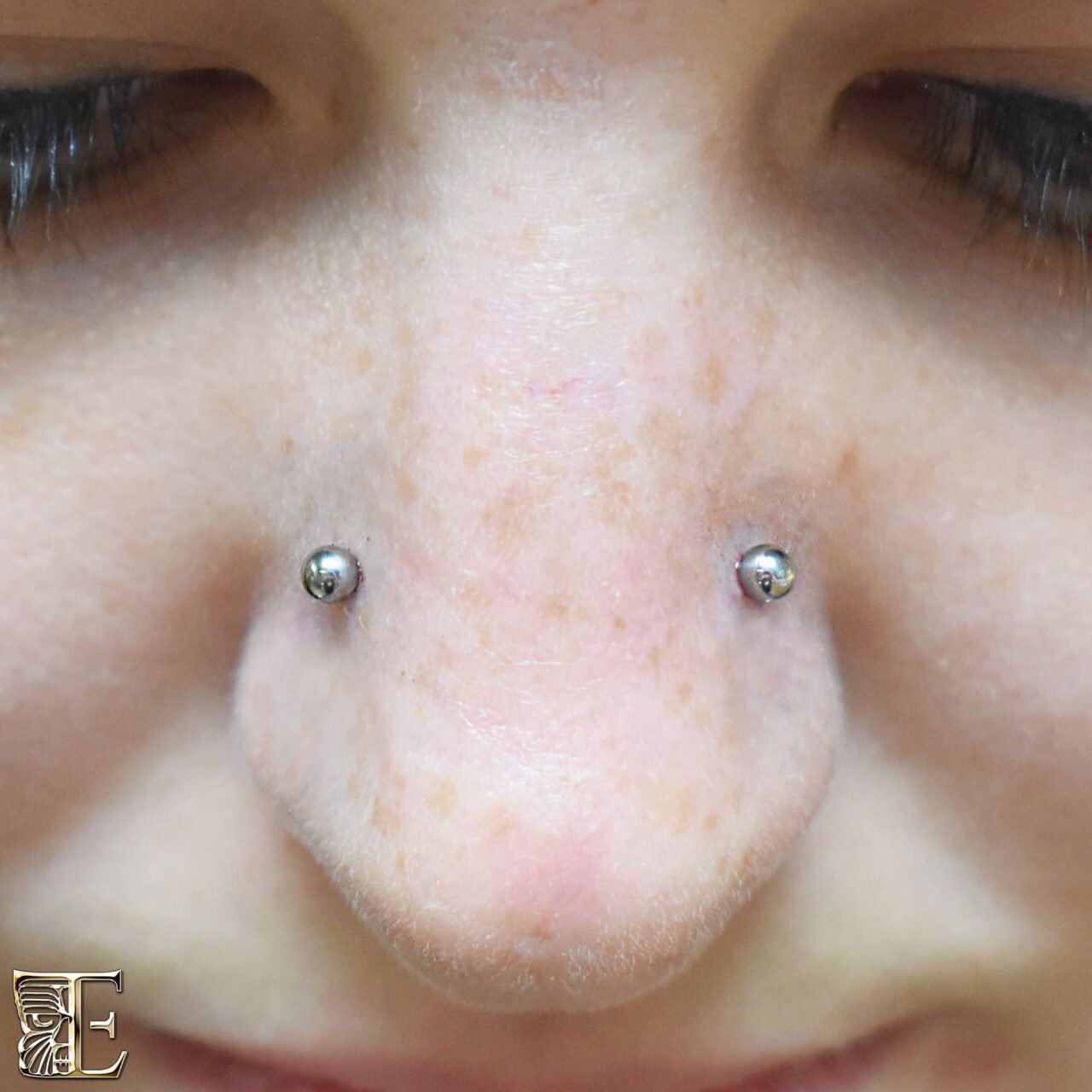 Forward-facing photo of a client with a beautiful pair of high nostril piercings, both styled with plain, minimalist implant-grade titanium studs made at Tribal Expression in Calgary