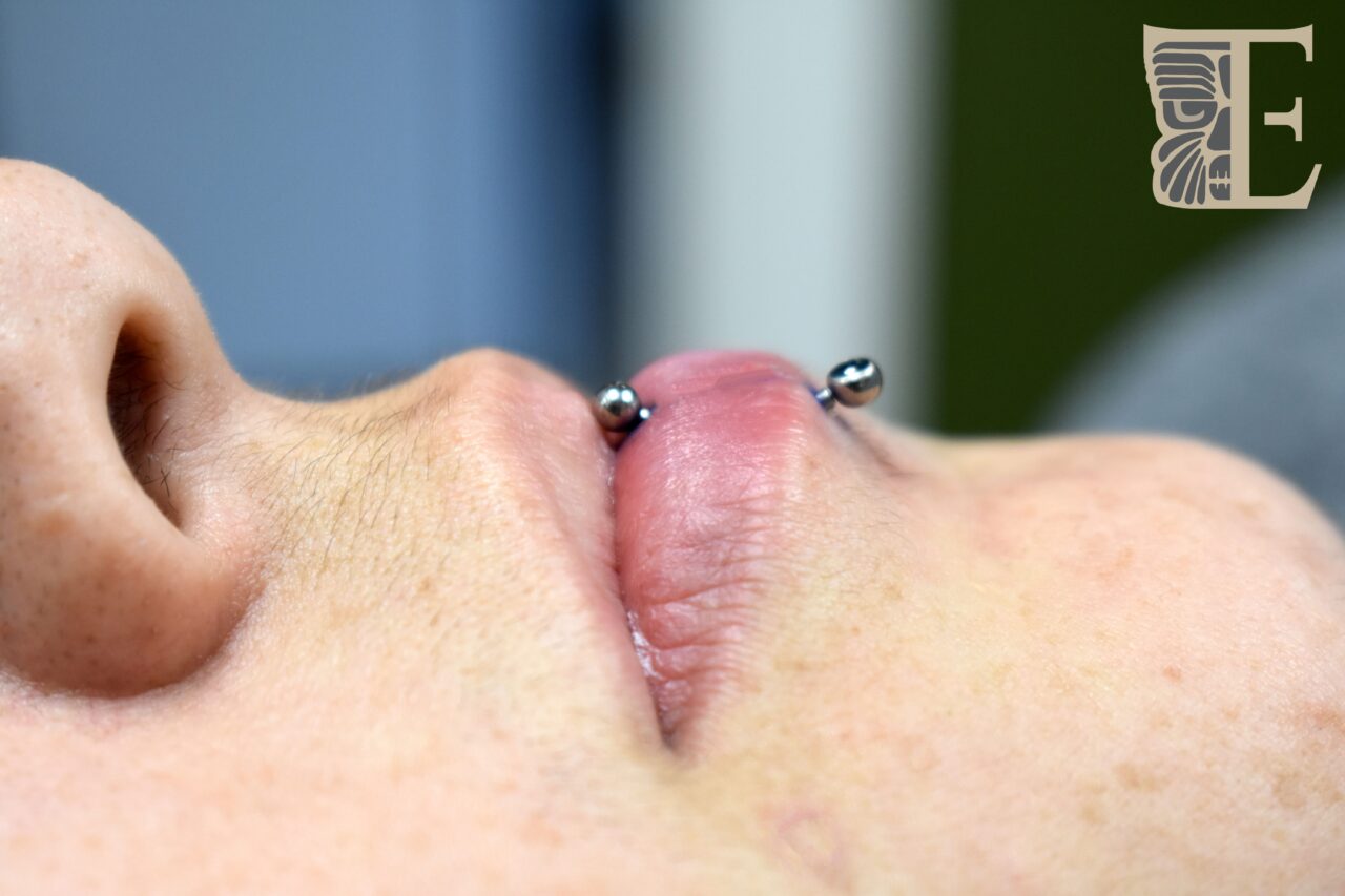 Side-profile photo of a person lying on their back with a single vertical lip piercing centered on the lower lip, featuring a sleek implant-grade titanium curved barbell, done at Tribal Expression in Calgary