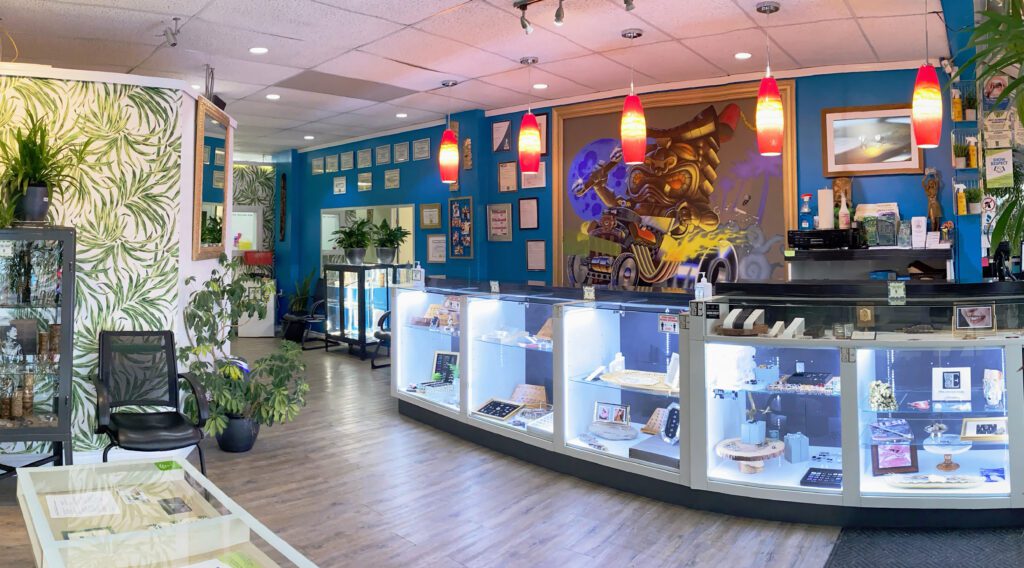 A wide angle photo of the front of the Tribal Expression store. It is displaying the background art behind the desk, as well as the jewellery and piercing certificates.