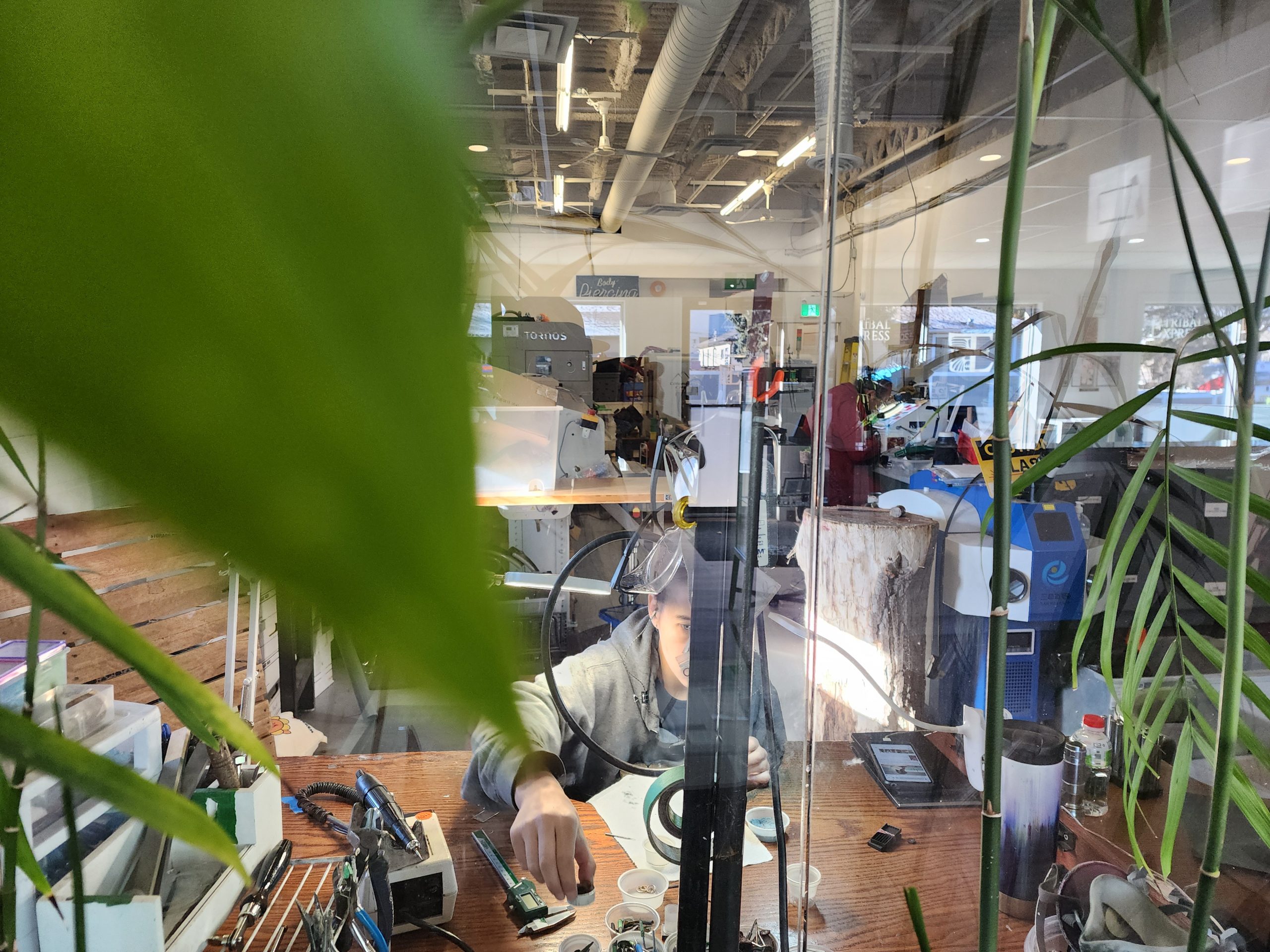 Tribal Expression goldsmith working in the in-house warehouse jewelry studio, visible through a window from the waiting room so clients can watch gold body jewelry being made in Calgary