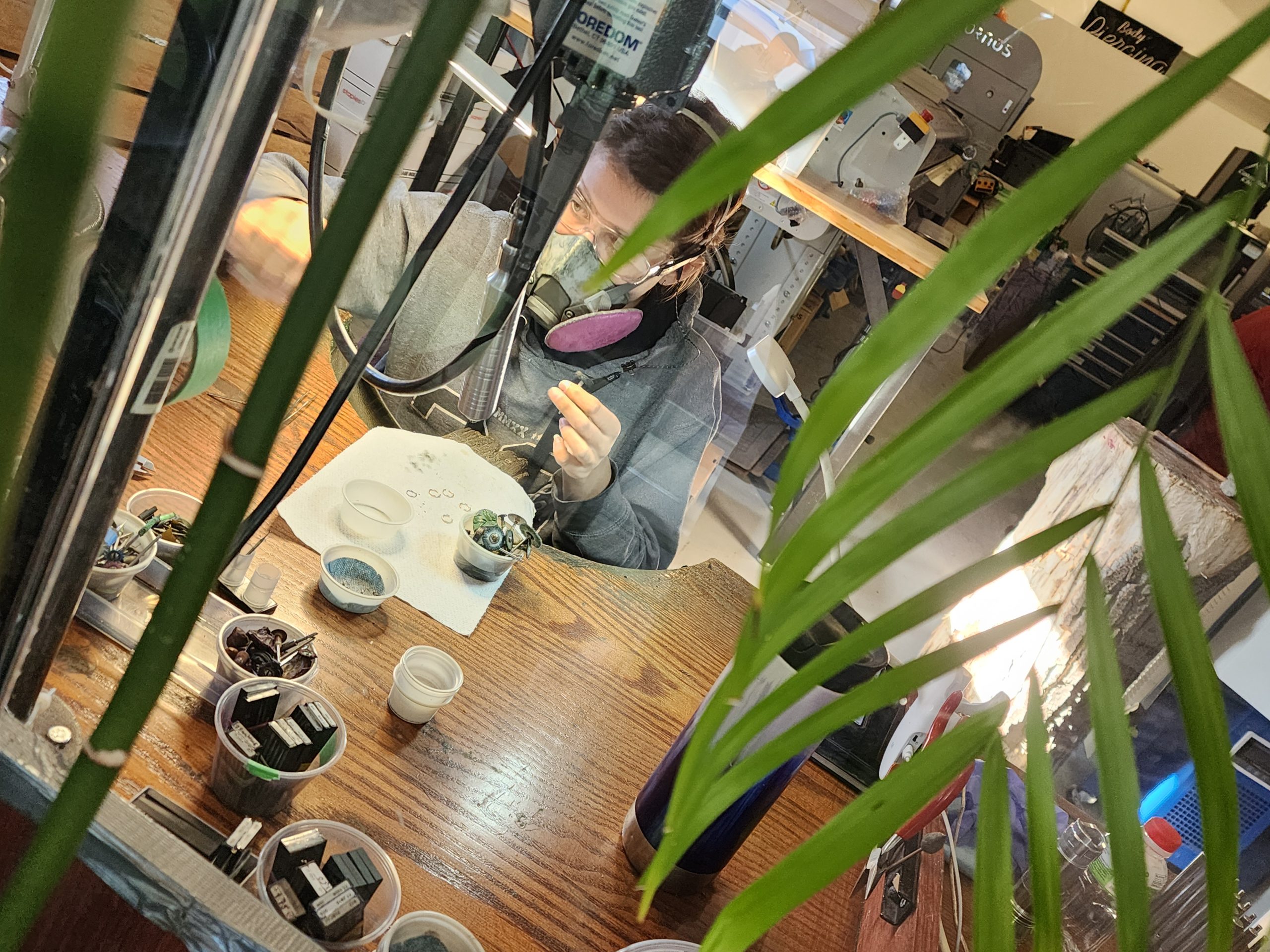 Goldsmiths handcrafting gold body jewelry at Tribal Expression in Calgary, seen through a workshop window visible from the waiting room, showcasing in-house jewelry design and manufacturing