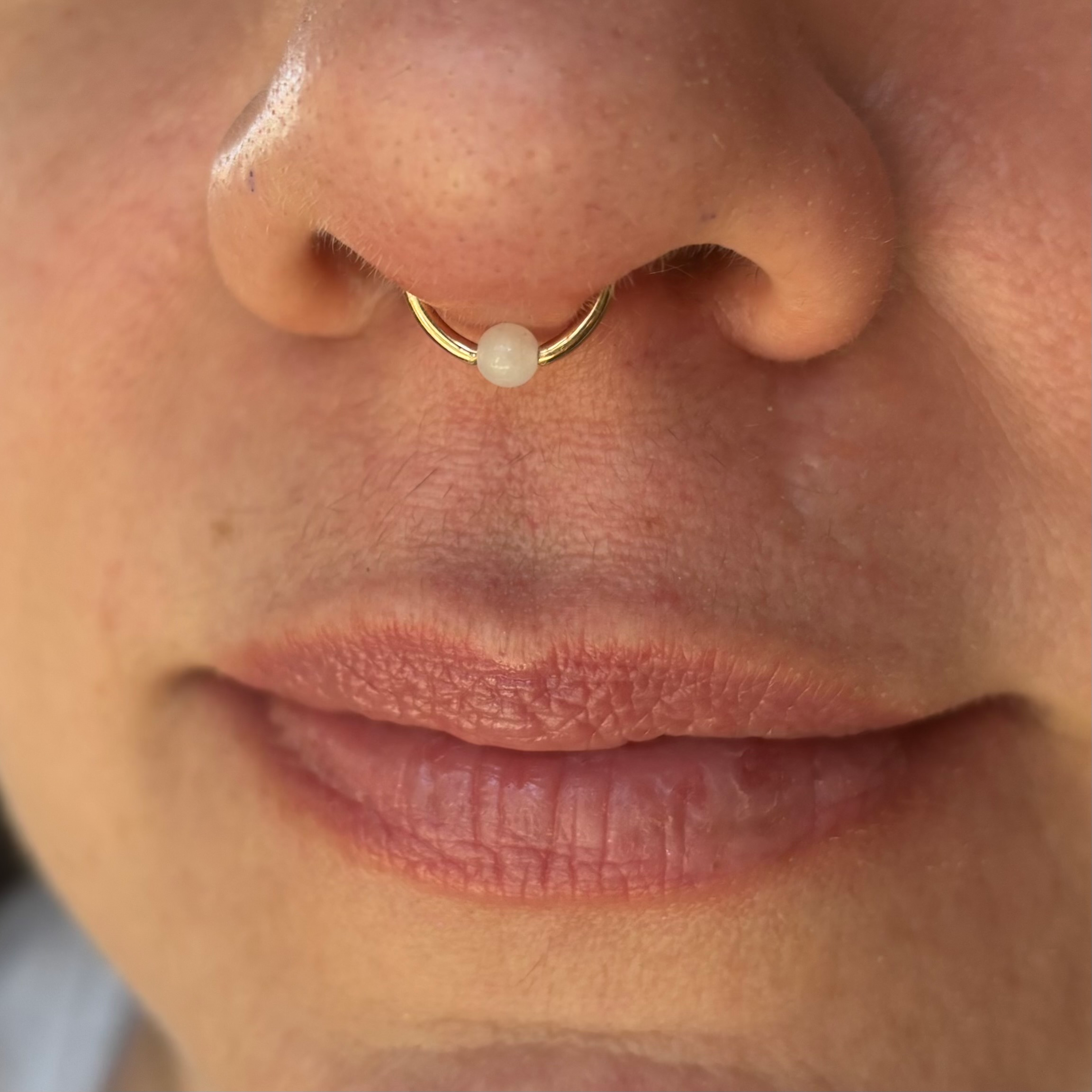 Gold Septum Piercing with White Quartz Bead – Tribal Expression Calgary Forward-facing photo of a beautifully centered septum piercing with a gold ring and white quartz bead, custom made at Tribal Expression in Calgary