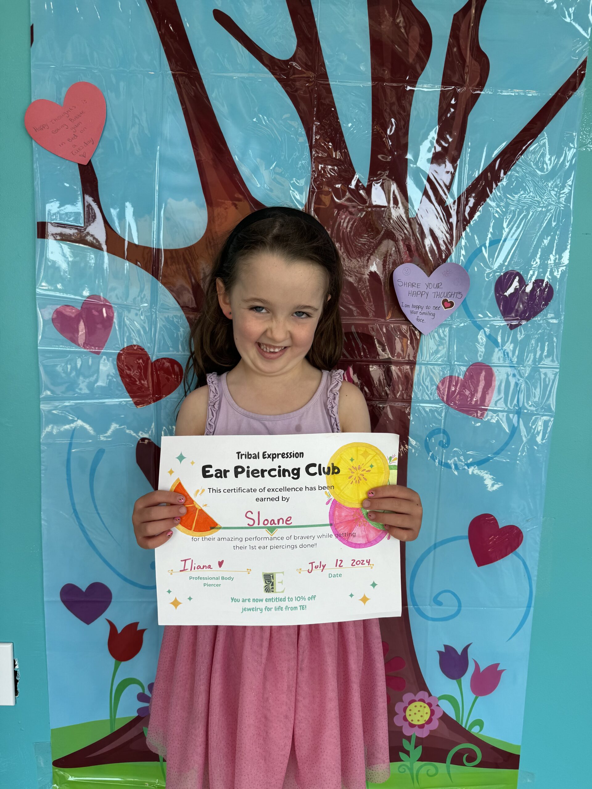 Very happy child holding an official ear piercing certificate after getting their ears pierced at Tribal Expression Kids in Calgary, a professional children’s ear piercing studio that uses safe, sterile techniques and high-quality jewelry